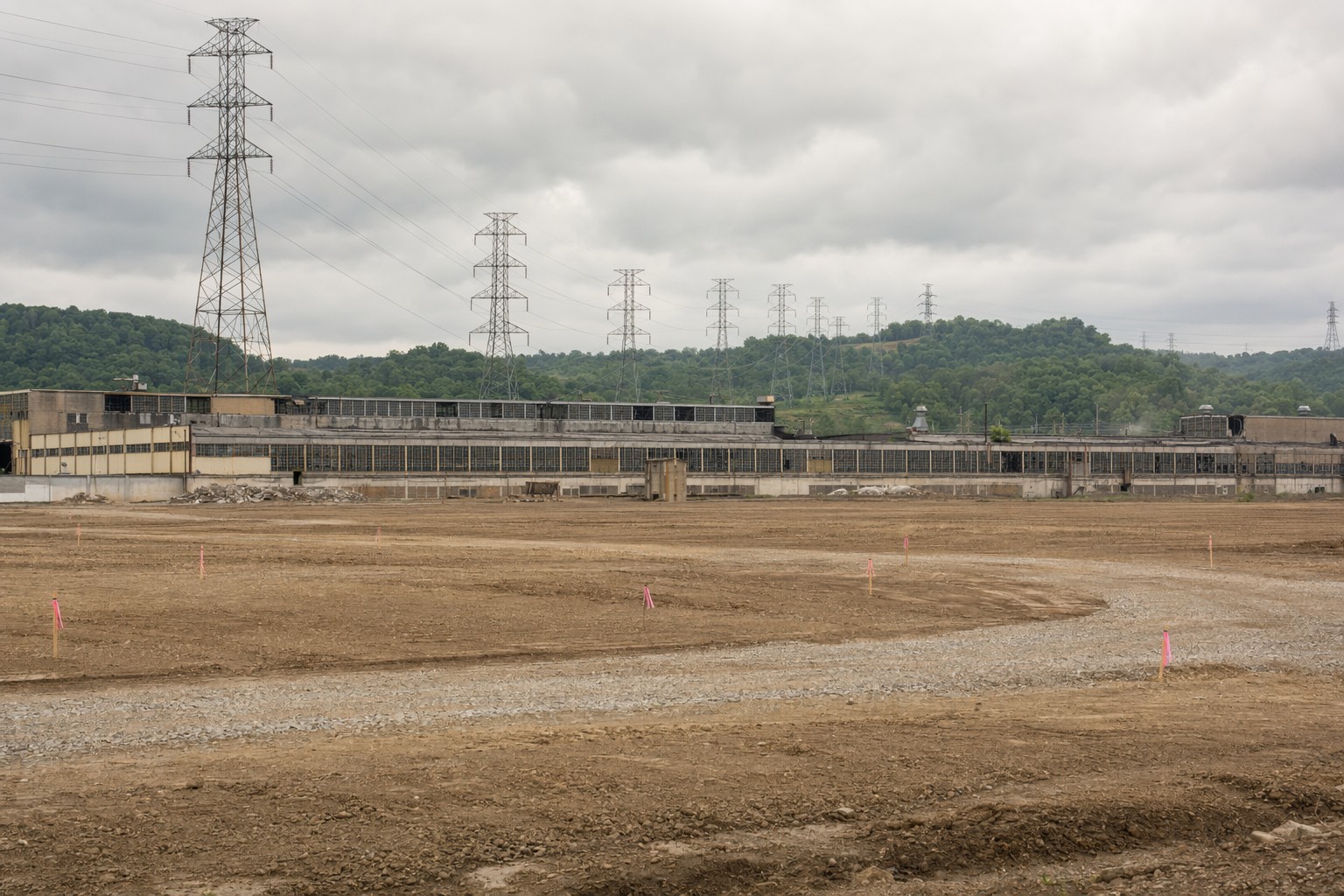 Cleared industrial site with a decommissioned plant building and transmission towers beyond